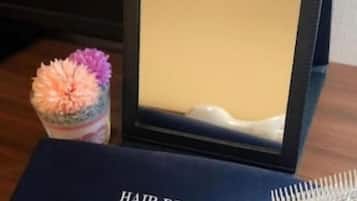 Ein Fön, ein Spiegel und eine Tasse mit Blumenmotiv auf einem Tisch.