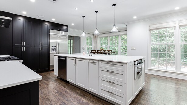 Une cuisine moderne avec des meubles de couleur sombre, des plans de travail blancs et un grand îlot central.