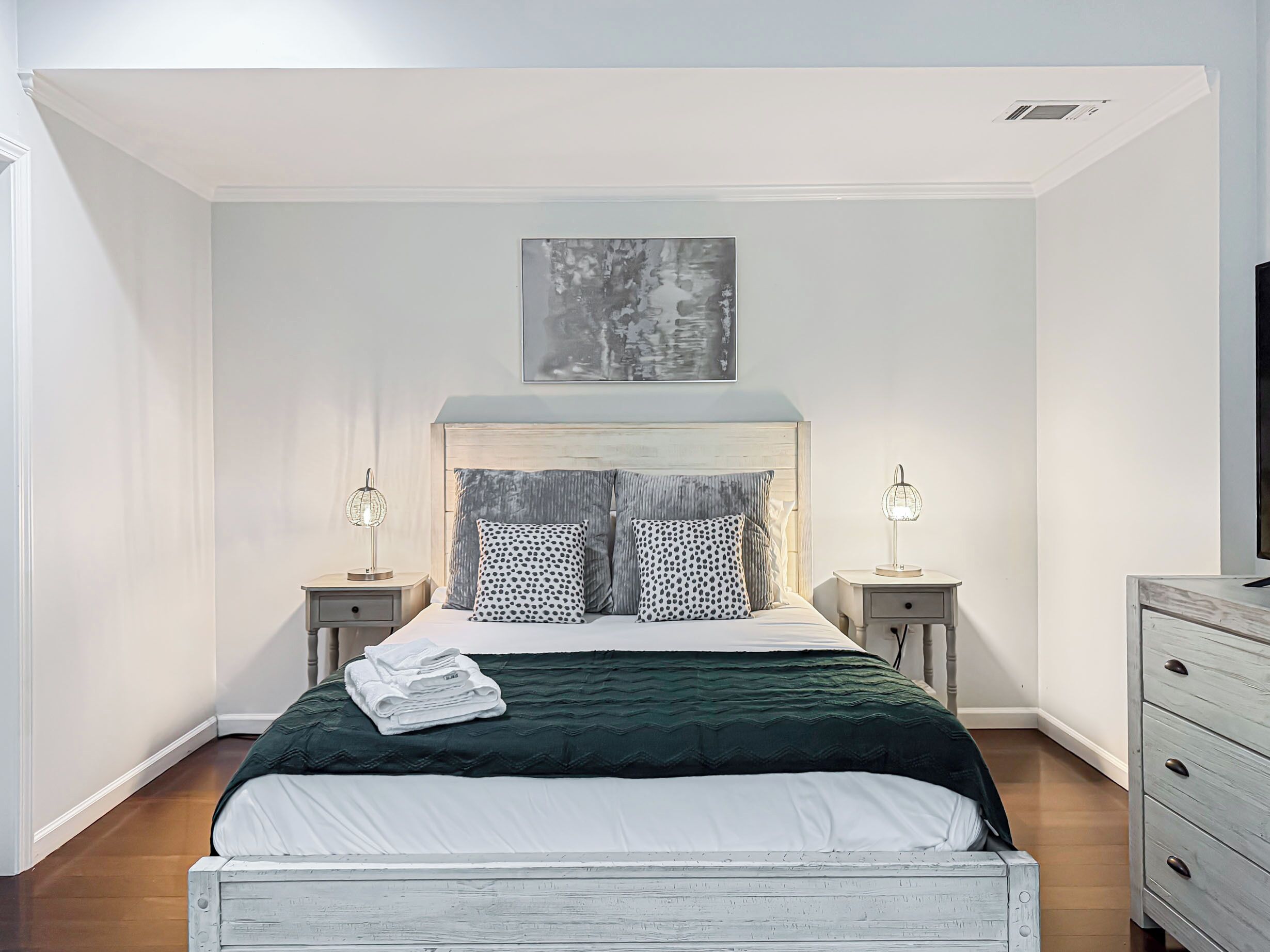 A bedroom with a bed, two bedside tables, a wall-mounted artwork, and a dresser.
