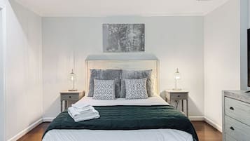 A bedroom with a bed, two bedside tables, a wall-mounted artwork, and a dresser.