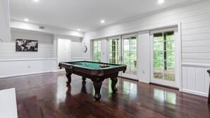 Une pièce spacieuse avec une table de billard, de grandes fenêtres et une vue sur la verdure environnante.