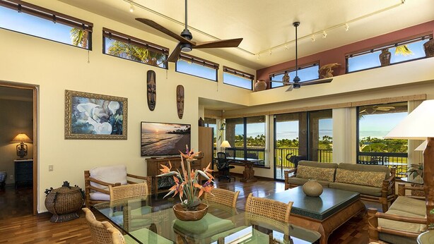 A spacious living area with a glass dining table, wicker furniture, and large windows offering views of the outdoors.