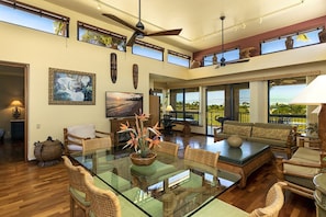 A spacious living area with a glass dining table, wicker furniture, and large windows offering views of the outdoors.