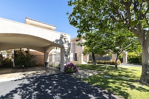 A residential area with a covered driveway, a tree, and a house with a number '23' on the wall.