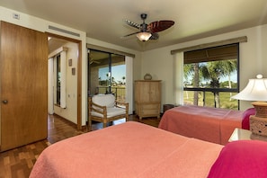 A hotel room with two beds, a ceiling fan, a view of the outdoors, and a wicker chair.
