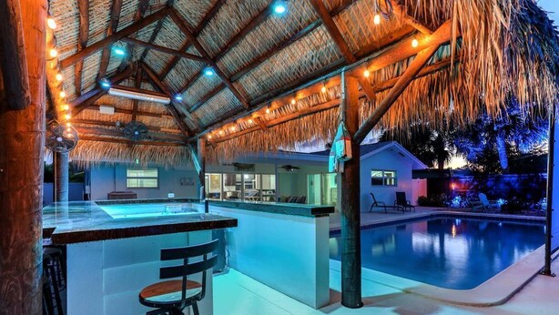 Zona bar con piscina, tetto di paglia e sgabelli da bar.