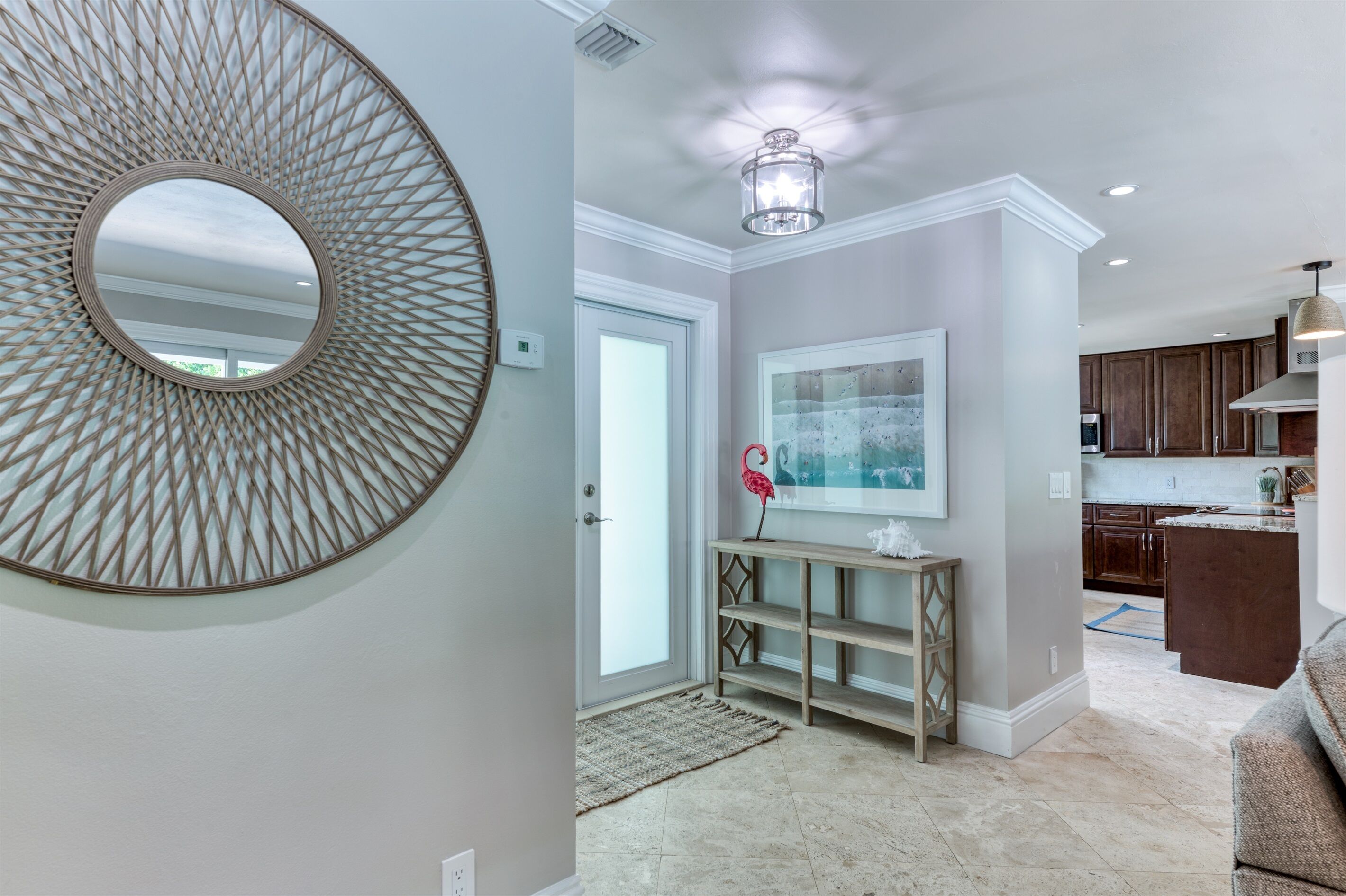 A modern interior with a round mirror, a wooden console table, and a kitchen area visible through an open door.