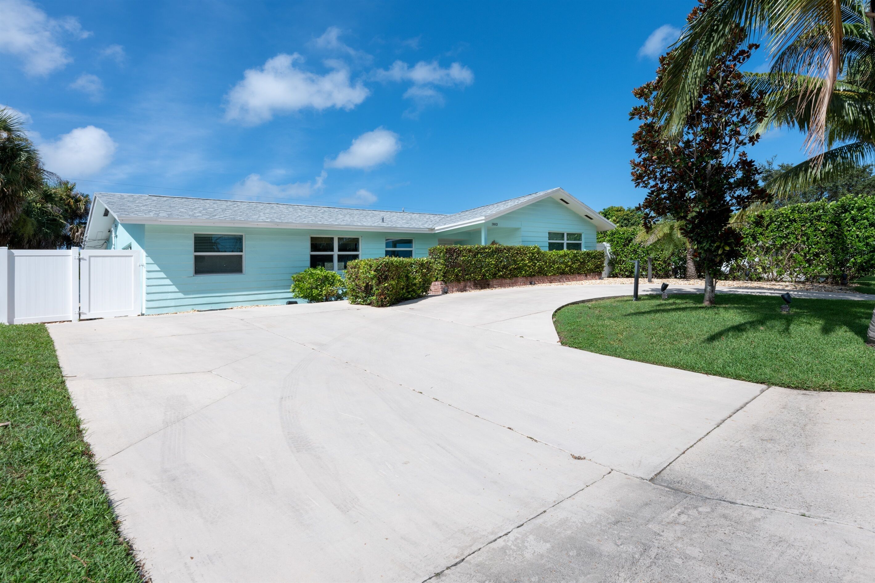 A light blue house with a white fence, a driveway, and a well-maintained lawn.