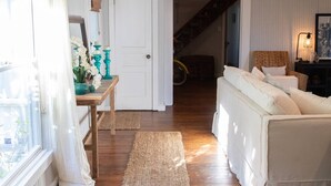 Una sala de estar acogedora con piso de madera, un sofá blanco, una mesita con objetos decorativos y una escalera que sube a otro nivel.