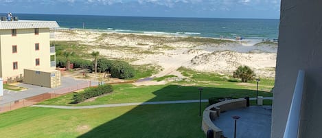 Uitzicht vanaf een balkon over een strand, grasvelden en een gebouw met een bord.