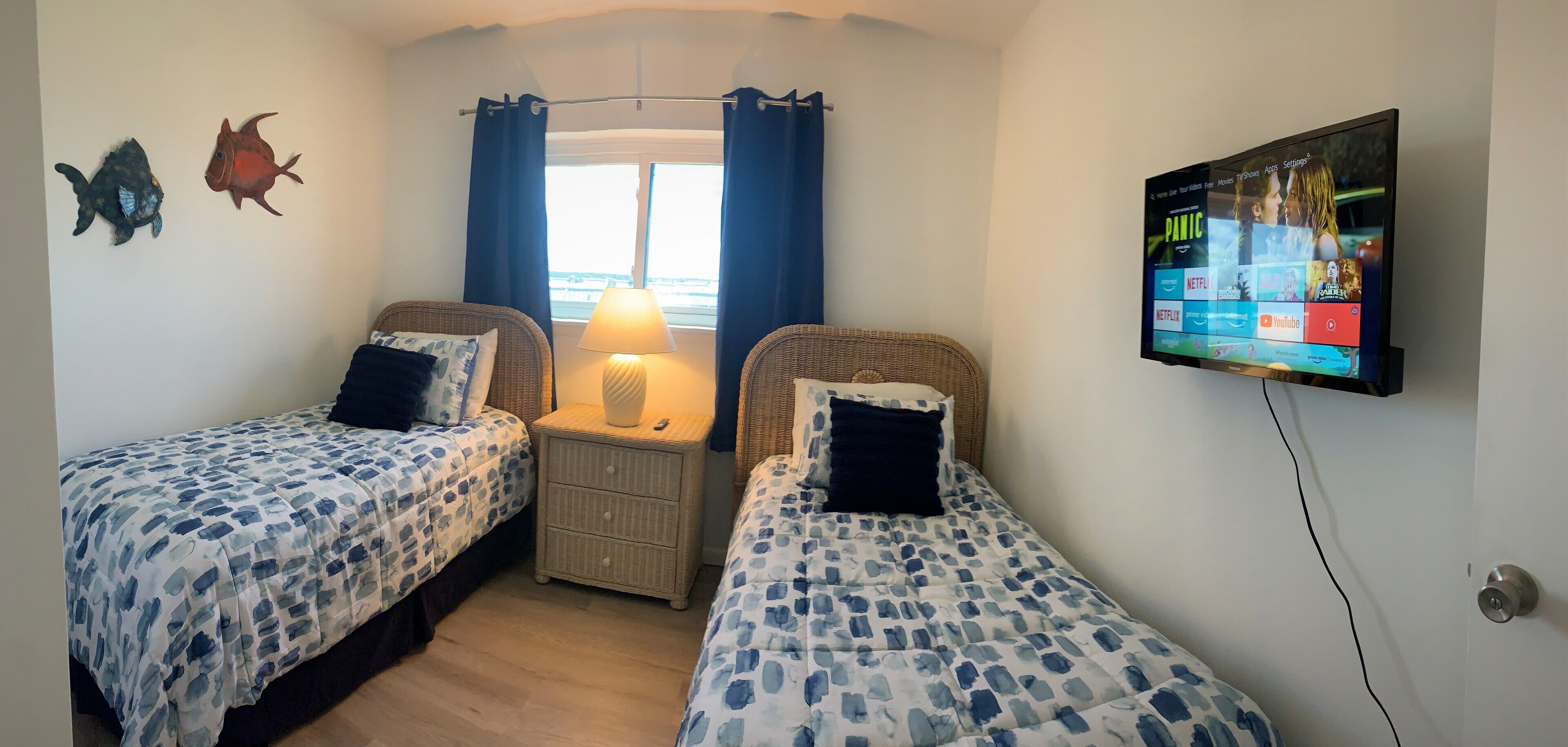A bedroom with two beds, a TV mounted on the wall, and a window with curtains.
