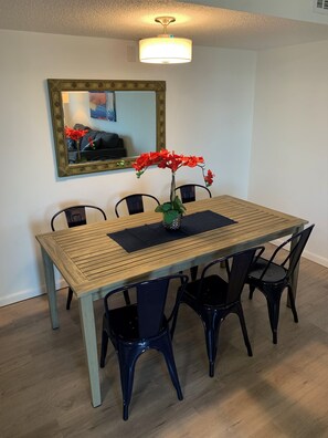 A dining area with a wooden table, black chairs, a vase with red flowers, and a mirror on the wall.