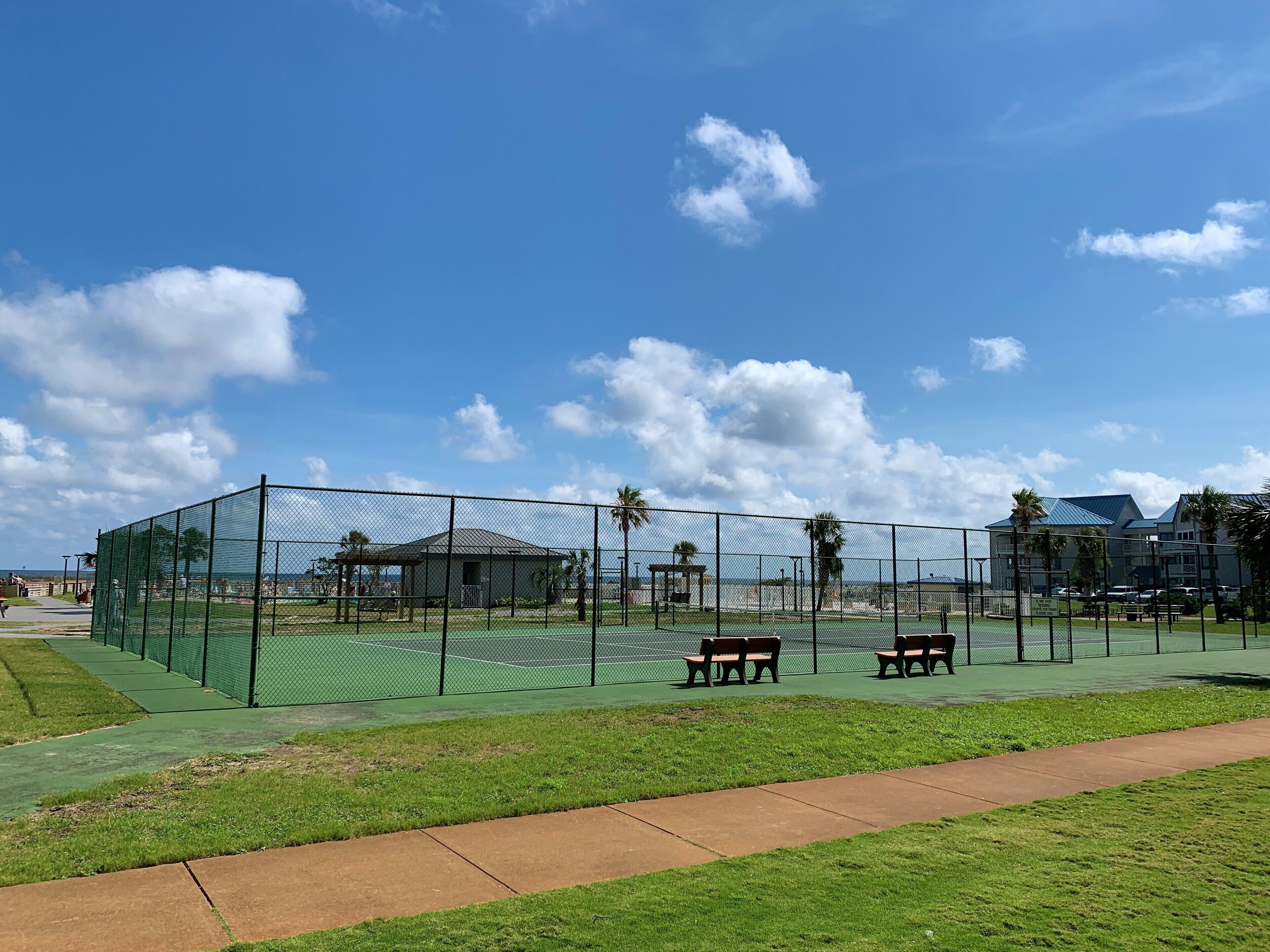 A fenced tennis court with benches and a clear sky.