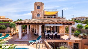 Una villa con piscina, mobiliario de exterior y una torre.