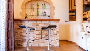 Una zona de bar con dos taburetes, una pared de piedra y un estante con botellas.