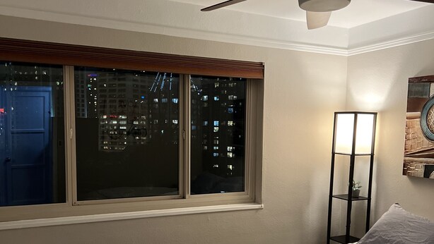 A bedroom with a bed, a ceiling fan, a window with a view of a cityscape, and a nightstand with a lamp. - 2 bedroom penthouse downtown Seattle (Seattle)