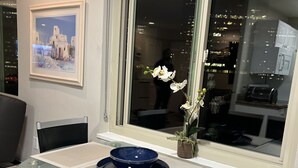 Un espace repas moderne avec une table en verre, des chaises noires et un vase contenant des fleurs blanches.