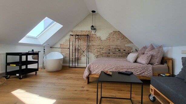 Un dormitori tipus loft amb sostre inclinat, paret de maó a la vista i una finestra de sostre.
