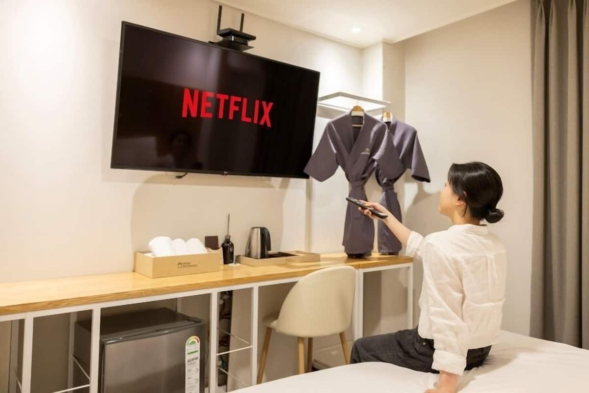 Una habitación de hotel con una cama, un escritorio con un televisor que muestra 'NETFLIX', un minibar y un armario con ropa.