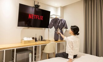 Una habitación de hotel con una cama, un escritorio con un televisor que muestra 'NETFLIX', un minibar y un armario con ropa.