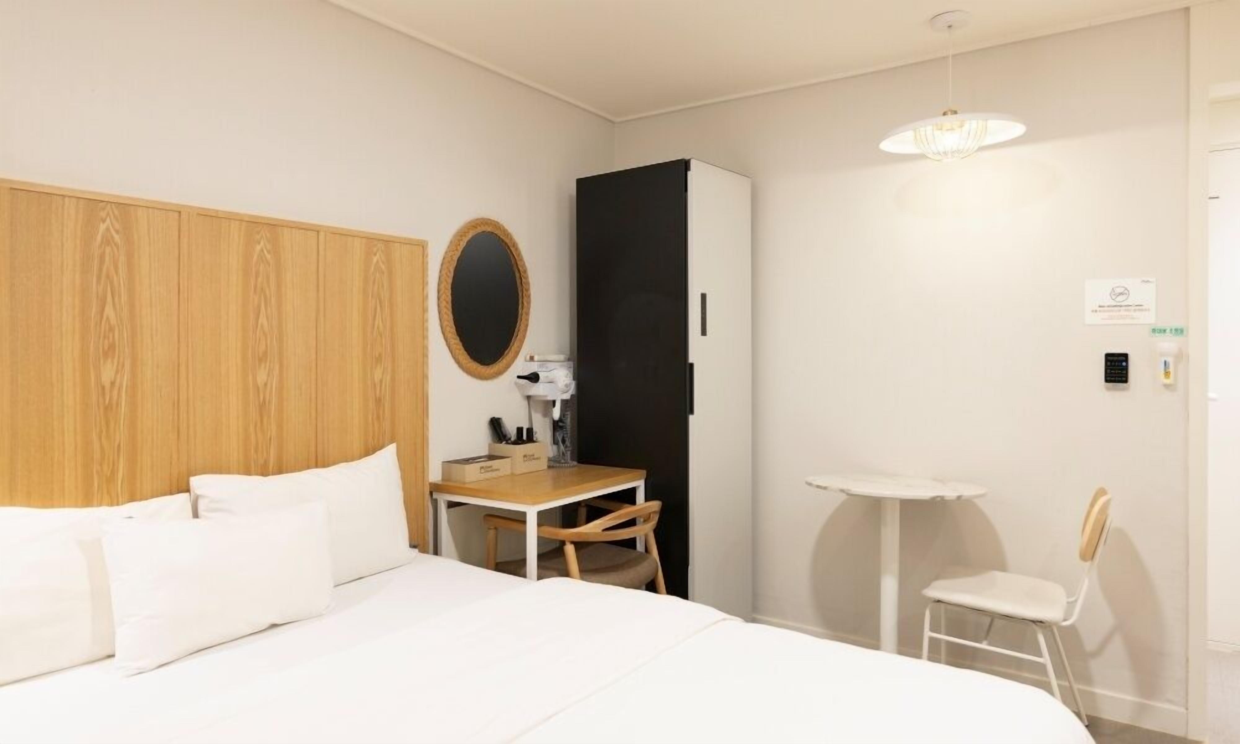 Une chambre d’hôtel comprenant un lit, un bureau, une chaise, une petite table, un miroir et un luminaire suspendu.