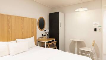 Une chambre d’hôtel comprenant un lit, un bureau, une chaise, une petite table, un miroir et un luminaire suspendu.