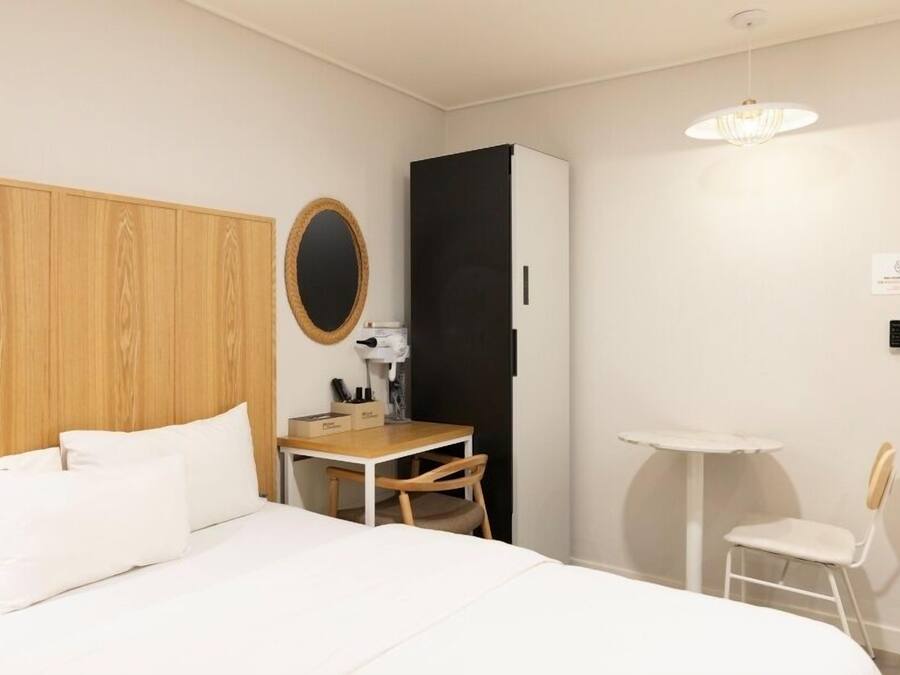 Une chambre d’hôtel comprenant un lit, un bureau, une chaise, une petite table, un miroir et un luminaire suspendu.