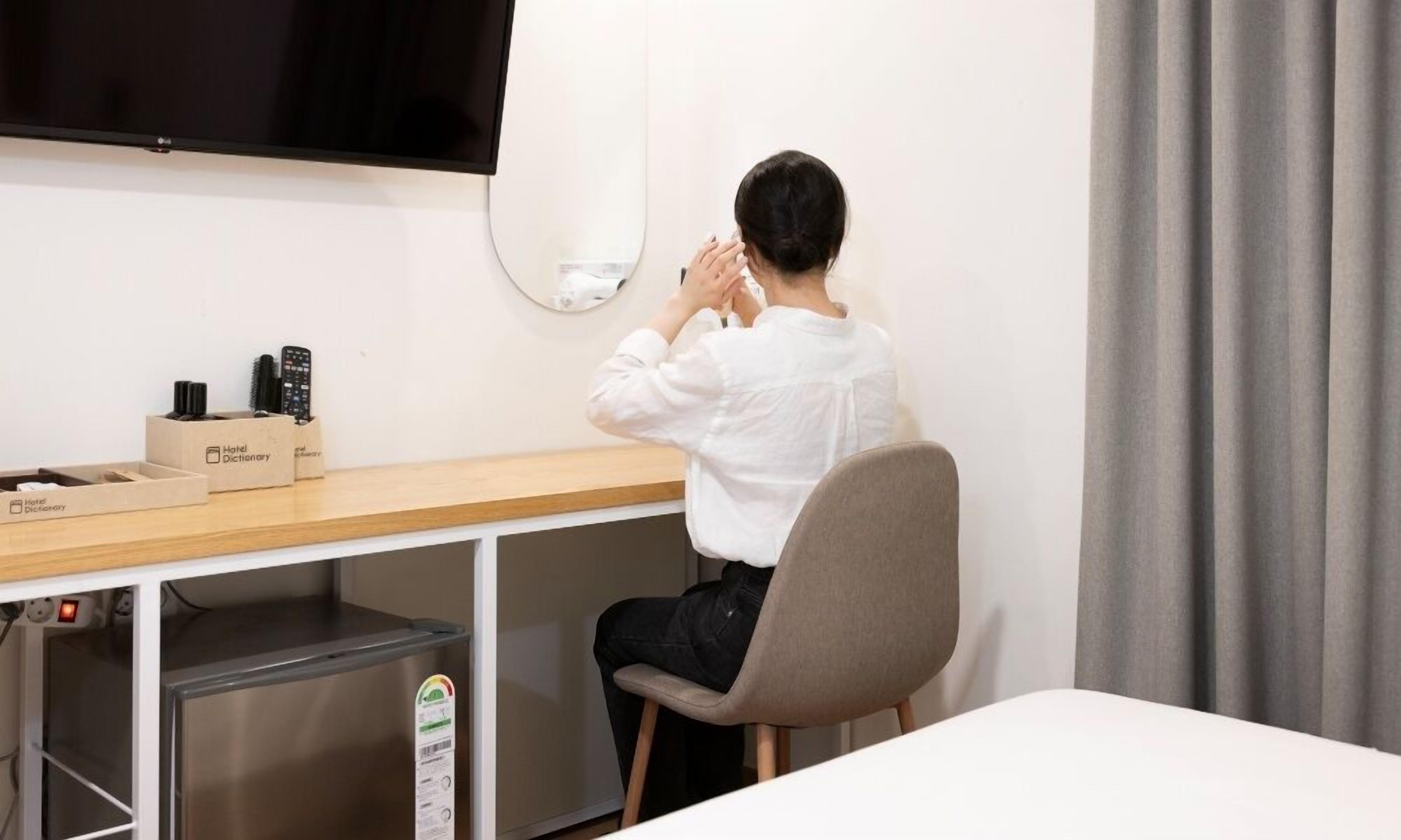 A hotel room with a desk, a television, a mirror, and a chair.