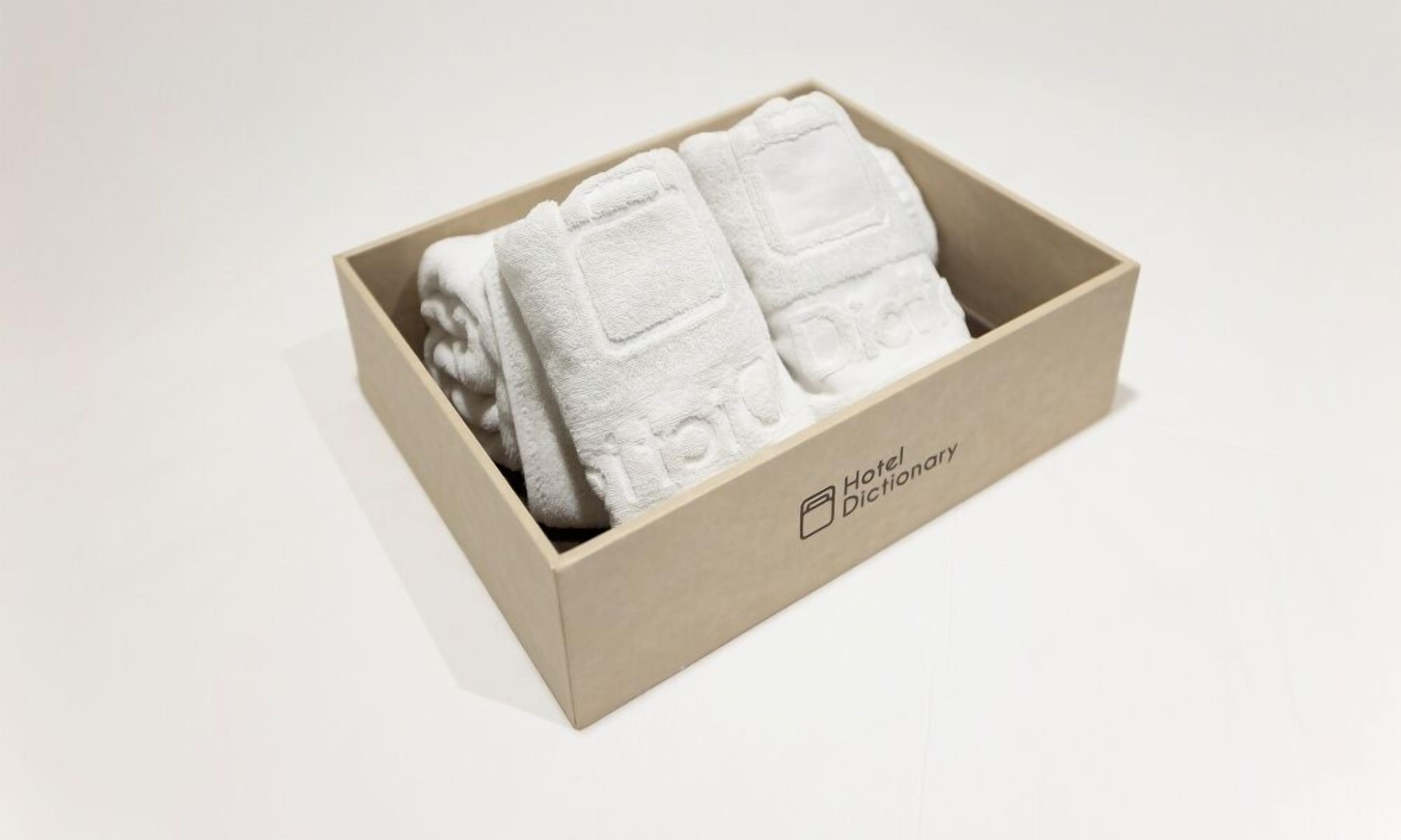 A wooden box containing folded white towels with embossed text, labeled "Hotel Dictionary."