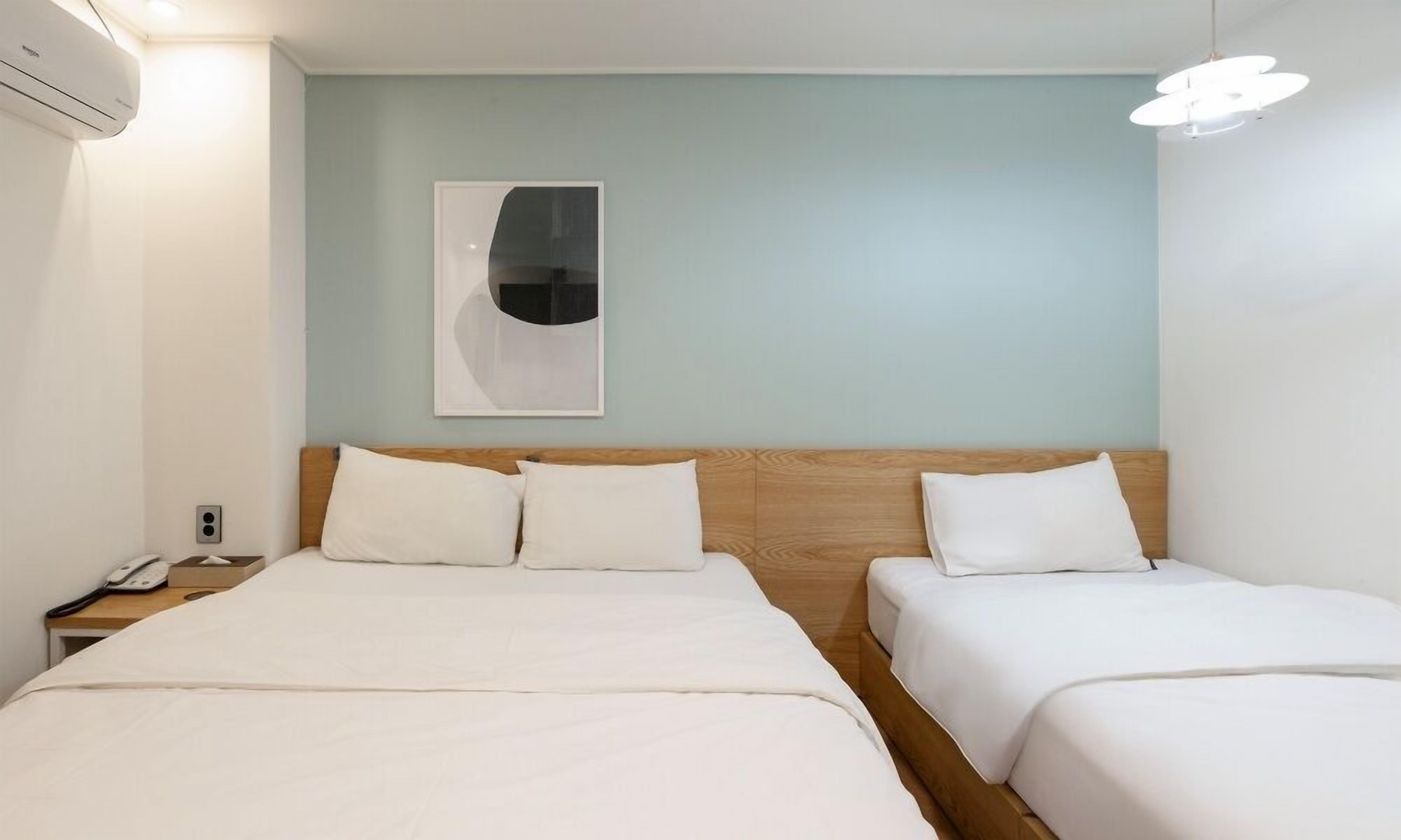 Habitació d'hotel amb dos llits, un capçal de llit de fusta, una taula de nit amb un telèfon i un aire condicionat fixat a la paret.