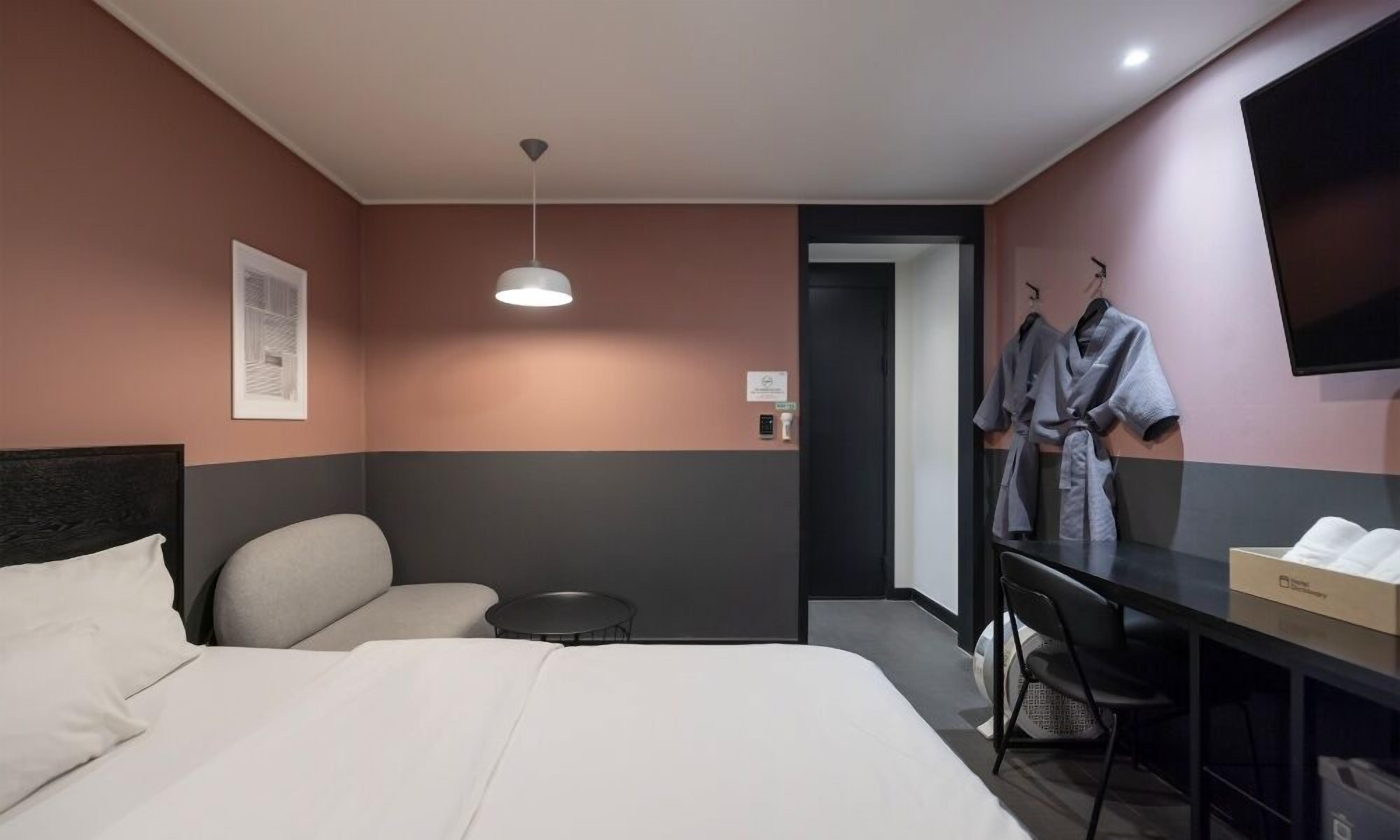 Una habitación de hotel con cama, escritorio, silla, perchero y televisor.
