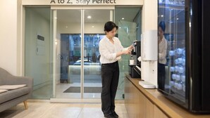 A person operating a coffee machine in a modern, well-lit indoor space with a glass entrance and a visible interior through the glass. - Cheongju Hotel Dictionary (Cheongju)
