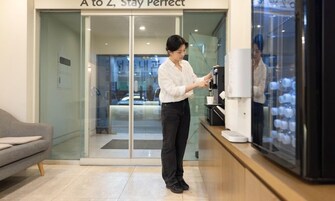 Una persona usando una máquina de café en un espacio interior moderno y bien iluminado, con acceso de vidrio y una vista al interior.