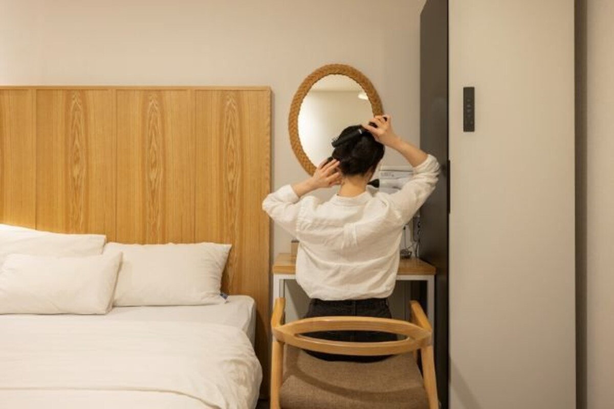A hotel room with a wooden headboard, a round mirror, a bed with white linens, and a small wooden chair.