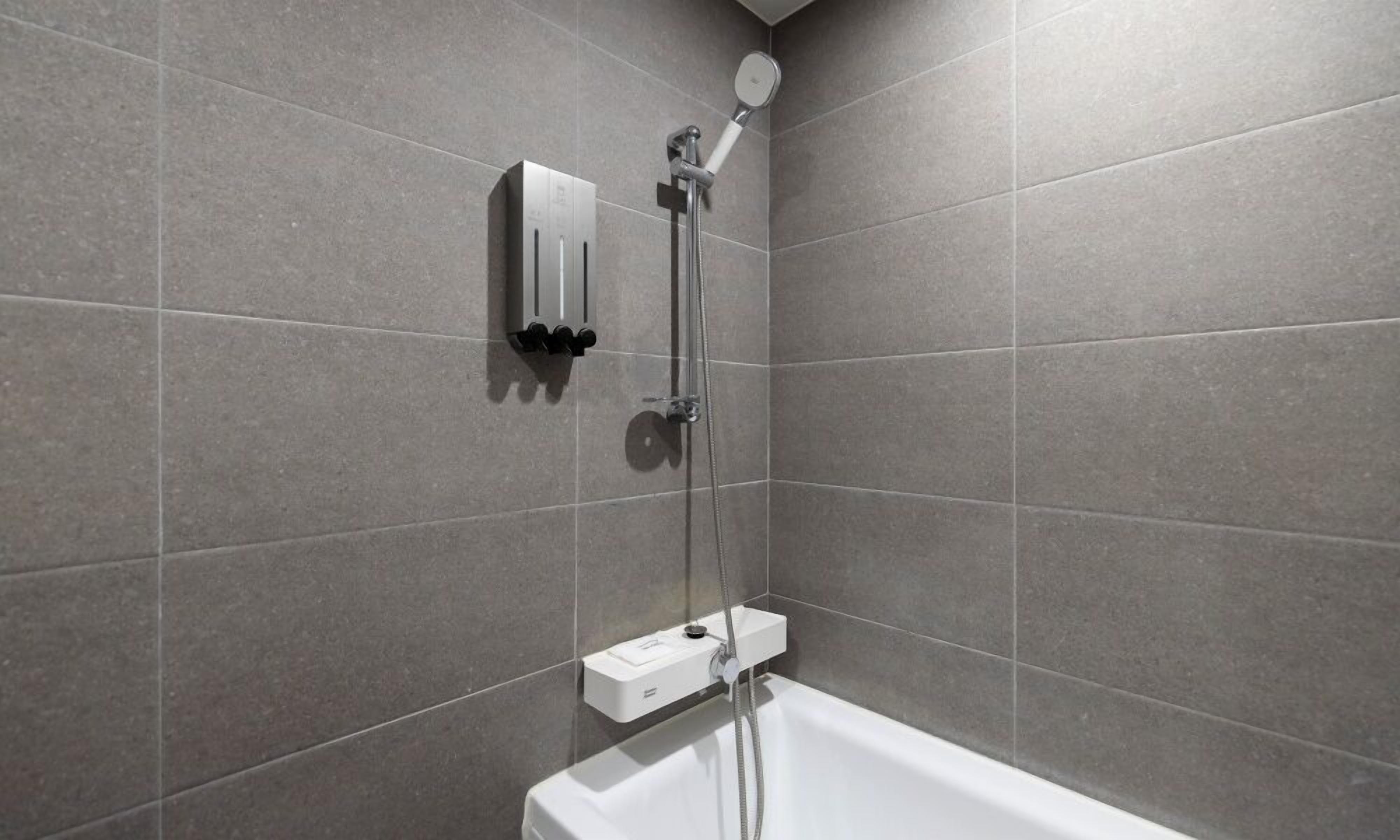 Un baño moderno con bañera, cabezal de ducha manual y panel de control en la pared.
