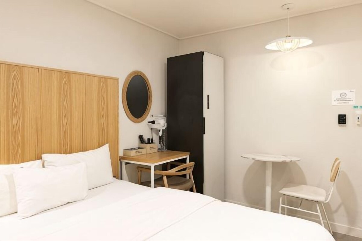 A hotel room with a bed, a desk, a chair, a wardrobe, and a small table.