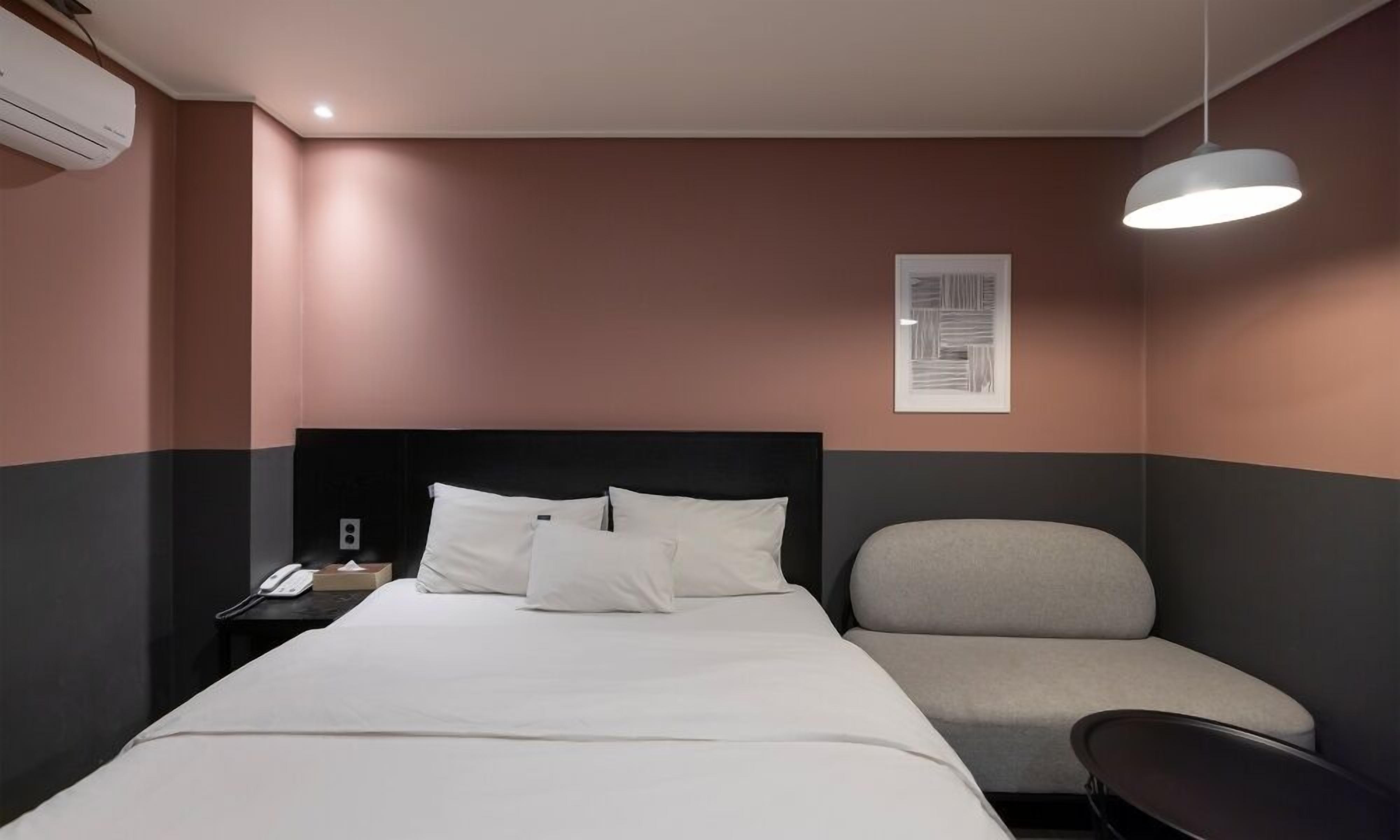 A modern hotel room with a bed, bedside table, lamp, and a chair.