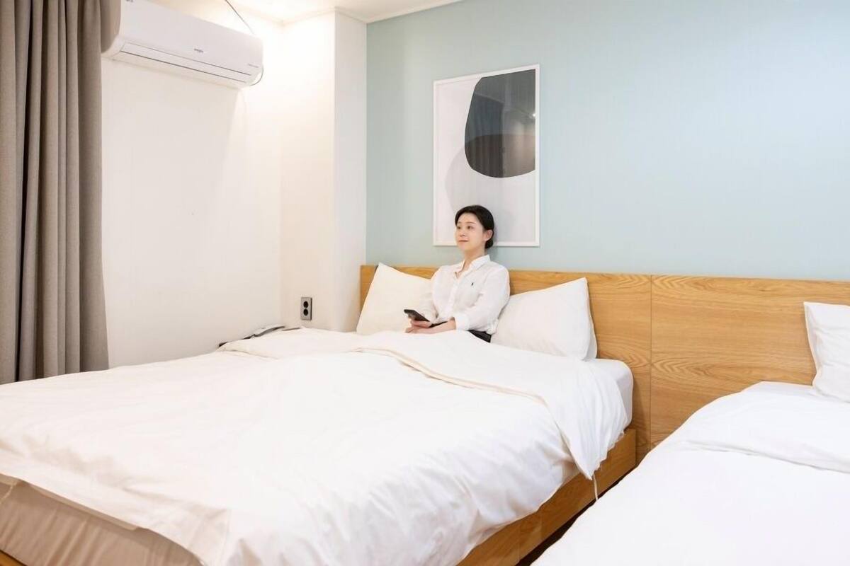 Una habitación de hotel con una cama grande, una cama más pequeña, un cabecero de madera, un aire acondicionado de pared y un cuadro en la pared.