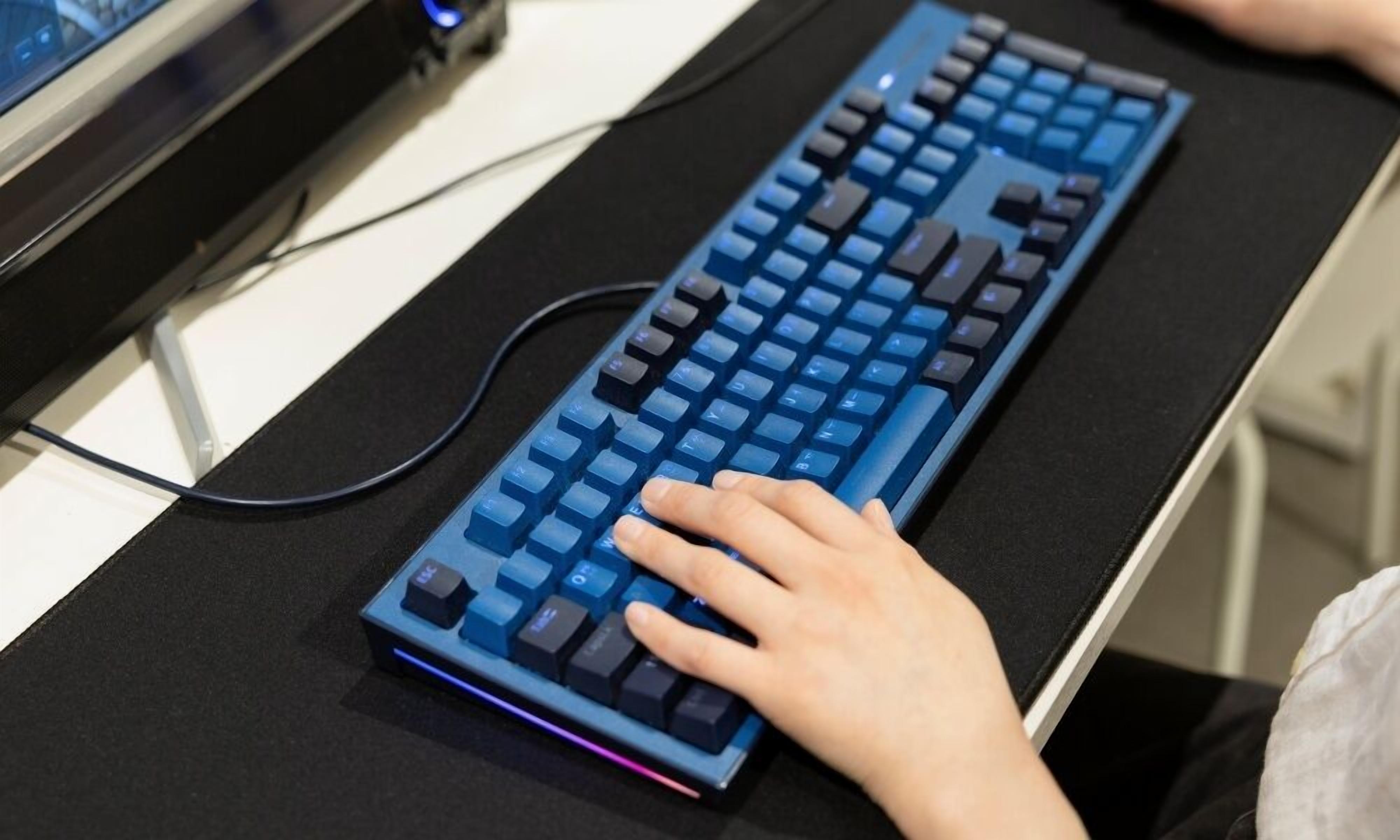 A person using a blue mechanical keyboard on a black desk.