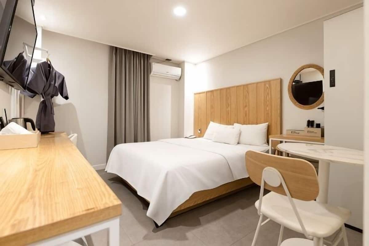 Una habitación de hotel con una cama, un escritorio, una silla, un televisor y un espejo.