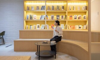 Una biblioteca moderna con una zona de asientos curva y una mesa de vidrio. Estanterías llenas de libros y revistas.