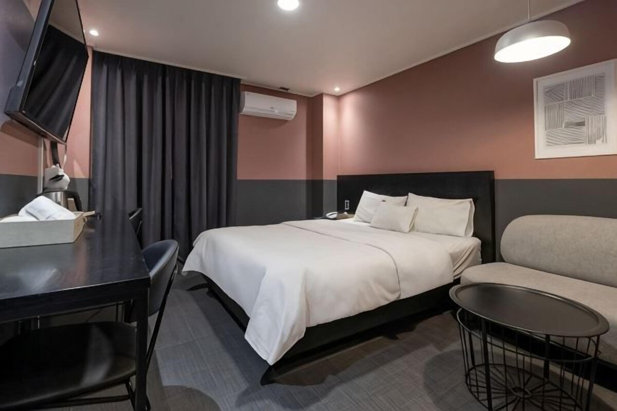 A hotel room with a bed, a sofa, a desk, and a TV.