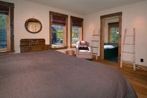 Quarto com uma cama grande, penteadeira, cadeira e escada encostada à parede.