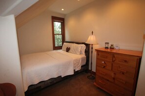 Un dormitorio con una cama individual, un aparador, una lámpara y una ventana.