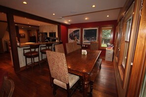 Un comedor con mesa y sillas de madera, una cocina al fondo y ventanas amplias con vistas.