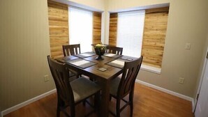 A dining area with a wooden table and chairs, two windows with blinds, and a vase with flowers on the table. - Culberhouse Cottage - Executive/Vacation Rental (Jonesboro)