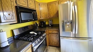 A kitchen with wooden cabinets, a stainless steel refrigerator, a microwave, a stove, and a coffee maker. - Culberhouse Cottage - Executive/Vacation Rental (Jonesboro)