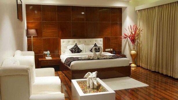 Quarto moderno com uma cama grande, sofás brancos, piso de madeira e um vaso decorativo.