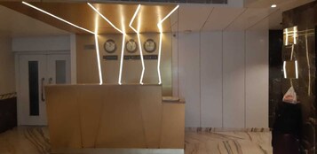 A reception area with a wooden reception desk, a wall clock, and a marble floor.