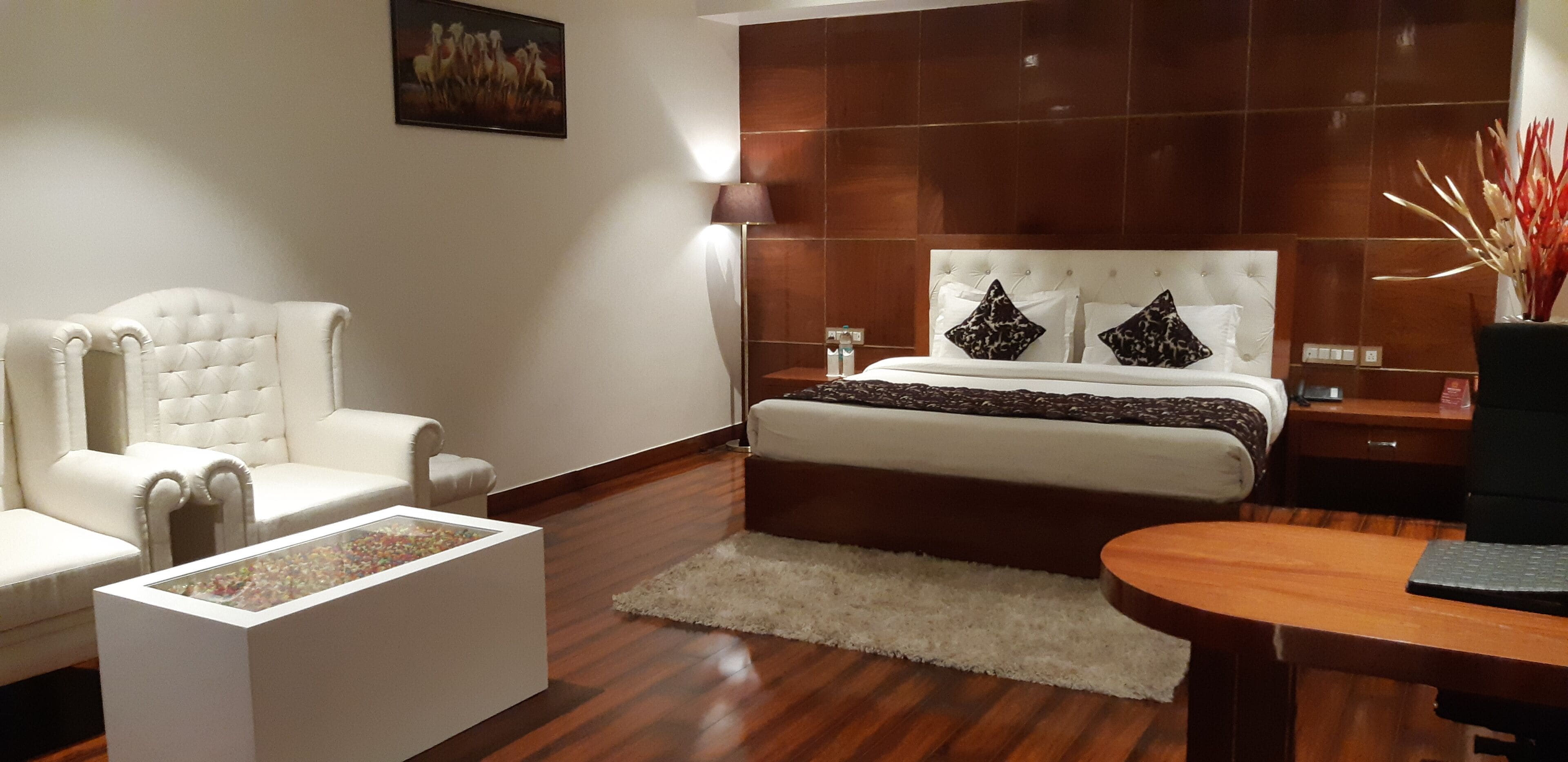 Een moderne slaapkamer met een groot bed, een witte fauteuil, een klein tafeltje en een decoratieve vaas.